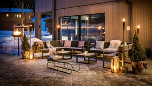 Een moderne buitenruimte met zitbanken, tafels en decoratieve lantaarns.