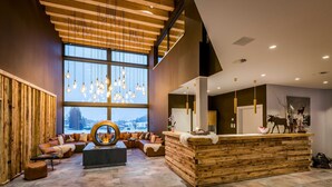 Een moderne lobby met een houten receptiebalie, een zithoek en grote ramen met uitzicht op het groen.