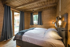A wooden cabin bedroom with a bed, curtains, and a hanging light fixture.
