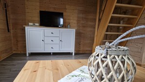 Ett rum med träpanel, ett vitt skåp, en platt-TV och en flätad korg som står på ett bord.