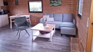 En mysig stuga med träpanel på väggarna, en grå soffa, ett matbord och en vit stol.