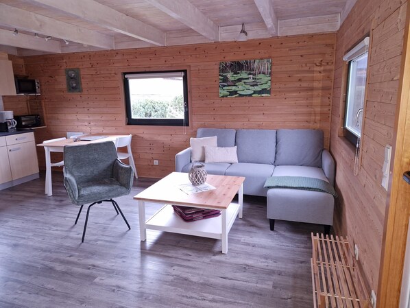 A cozy cabin interior with a wooden interior, a gray sofa, a dining table, and a white chair. - House 1 - lakesearch on Labussee (Userin)
