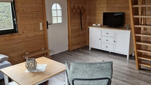 Ett mysigt rum med träväggar och trägolv, en vit dörr med ett fönster, en tv på ett träskåp och en stol med en kudde.