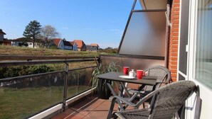 En balkon med et bord og stole, gelænder af glas, og udsigt til huse i baggrunden.