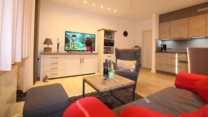 En moderne stue med et fladskærms-tv, en grå sofa, en rød skammel og et træsofabord.