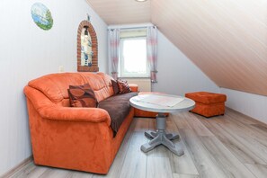A cozy room with a large orange sofa, a small round table, and a window with curtains.