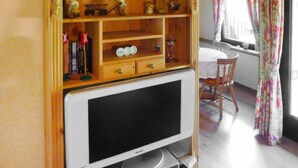 Una habitación con un mueble de televisión de madera, un televisor blanco, una mesa de comedor con sillas y una ventana con cortinas.