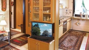 Cocina compacta con armarios de madera, televisor integrado y ventana con vistas a árboles.