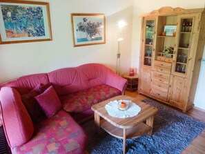 Ein Wohnzimmer mit einem rosafarbenen Sofa, einem Holzkabinett und zwei gerahmten Kunstwerken an der Wand.