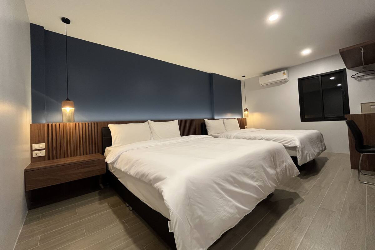 Moderni hotellihuone, jossa on kaksi sänkyä, puiset päätyosat ja sisäänrakennettu työpöytä tuolilla.
