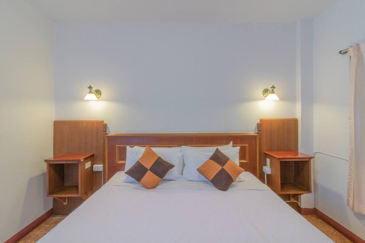Hotellihuone, jossa on puinen sängynpääty, kaksi yöpöytää ja kaksi seinään kiinnitettyä lamppua.