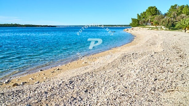 Une plage de galets bordée d’une eau d’un bleu limpide et d’une côte qui s’étend à perte de vue.