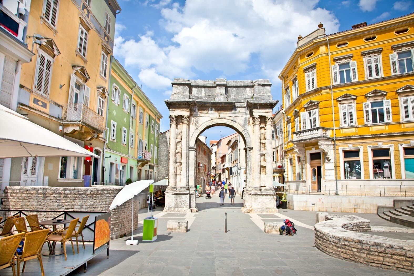 An ancient archway in a historic city center with colorful buildings on either side.
