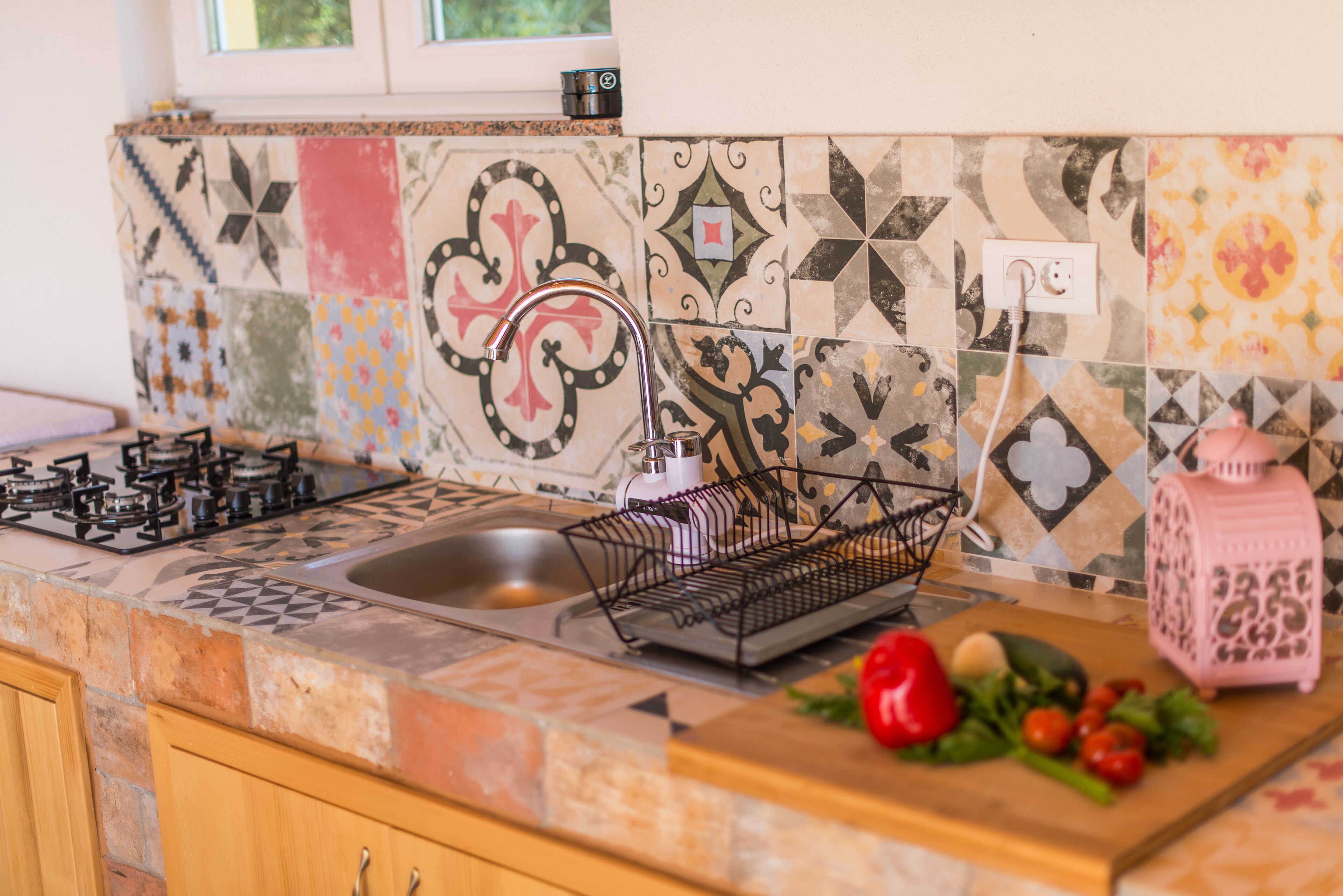 Una cocina con salpicadero de azulejos, estufa a gas, lavaplatos y escurreplatos.