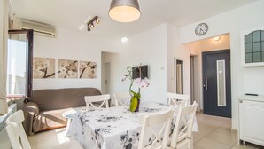 Un coin repas avec une table ronde, des chaises blanches, un vase de fleurs et une horloge murale.