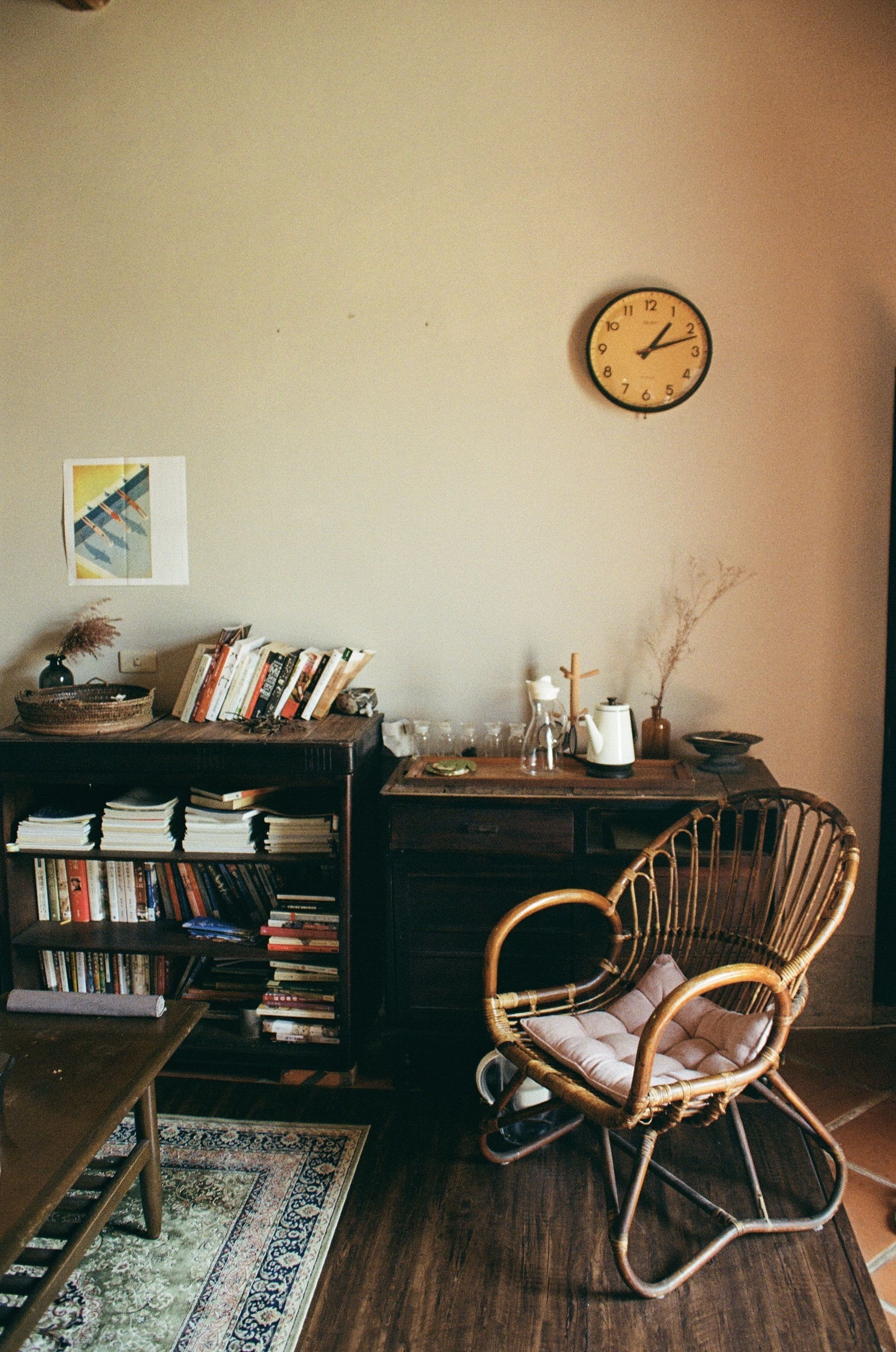 Une pièce chaleureuse avec un bureau en bois, une chaise en osier, une bibliothèque remplie de livres et une horloge murale.