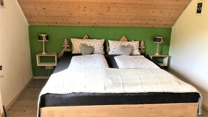 Ein Doppelbett mit weißer und schwarzer Bettdecke, zwei Nachttische mit Lampen sowie eine grüne Wand und eine Holzbodenverkleidung.