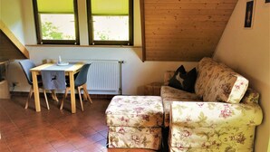Ein gemütliches Zimmer mit Holzbalkendecke, einem Esstisch mit Stühlen, einer Couch und einer Heizung.