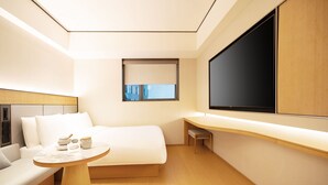 A modern hotel room with a bed, a small table, a sofa, a desk, and a large window. - Ji Hotel Orchard Singapore (Singapore)