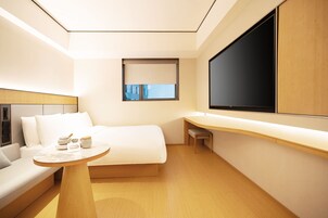 Habitación de hotel moderna con cama, una mesita, un sofá, un escritorio y un ventanal grande.