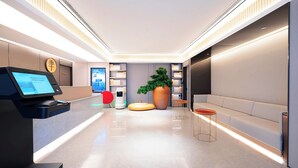 A modern hotel lobby with a reception desk, digital display, seating area, and a large potted plant. - Ji Hotel Orchard Singapore (Singapore)