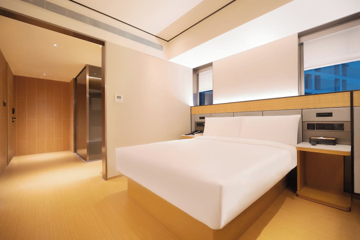 A modern hotel room with a large bed, a bedside table, and a built-in TV.