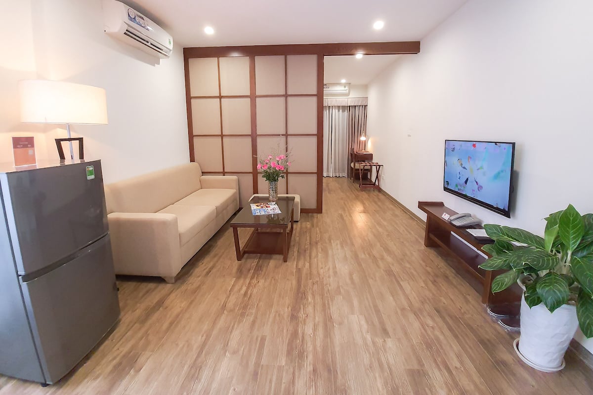 A modern living room with a sofa, a coffee table with a vase, a TV, and a refrigerator.