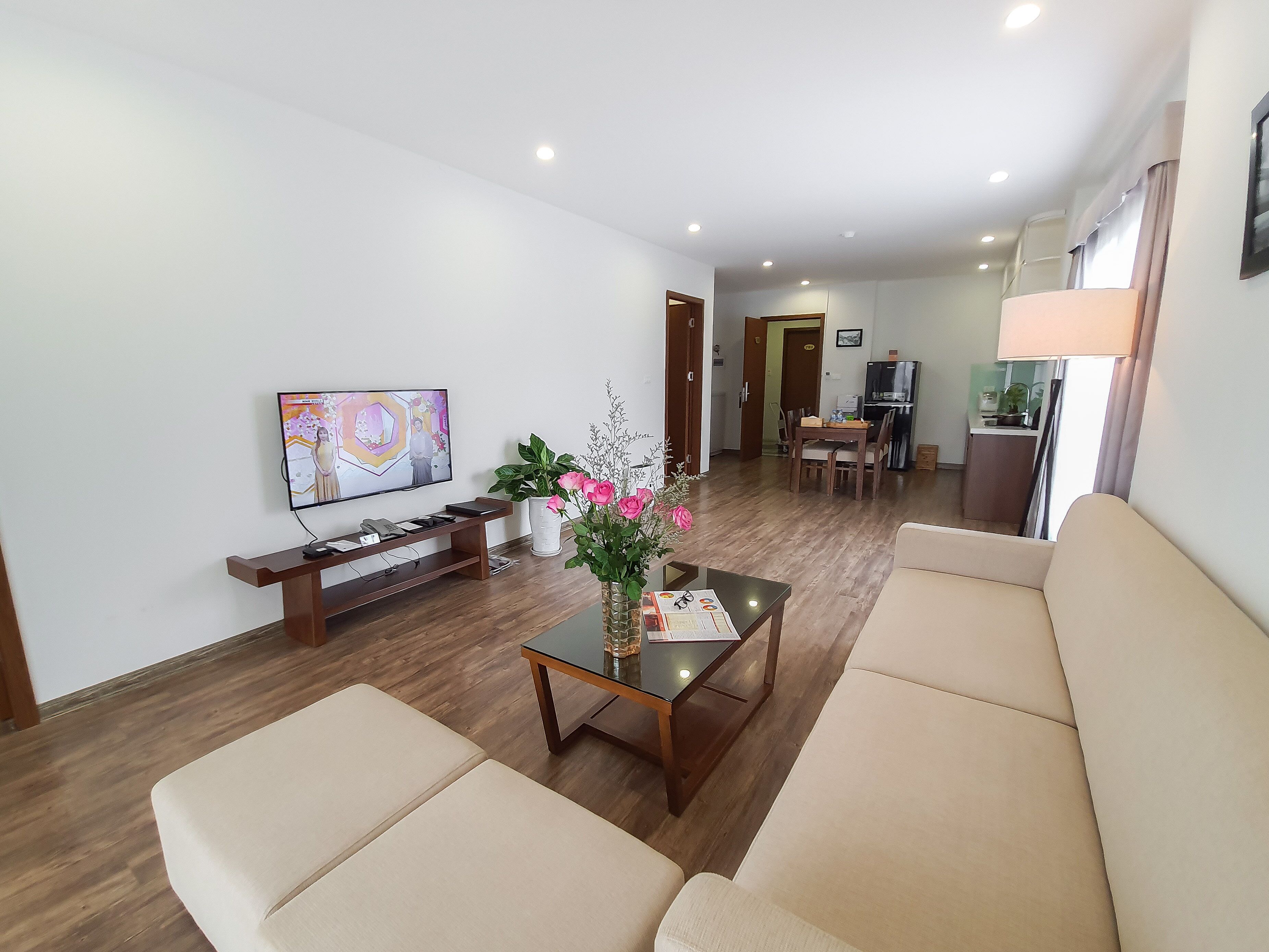 A living room with a TV, sofa, coffee table, and a dining area in the background.