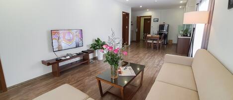 A living room with a TV, sofa, coffee table, and a dining area in the background.