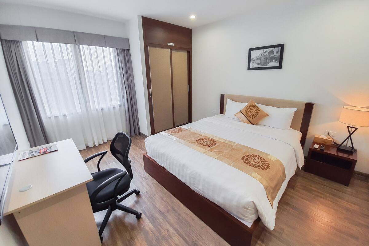 A hotel room with a bed, desk, chair, and a picture on the wall.