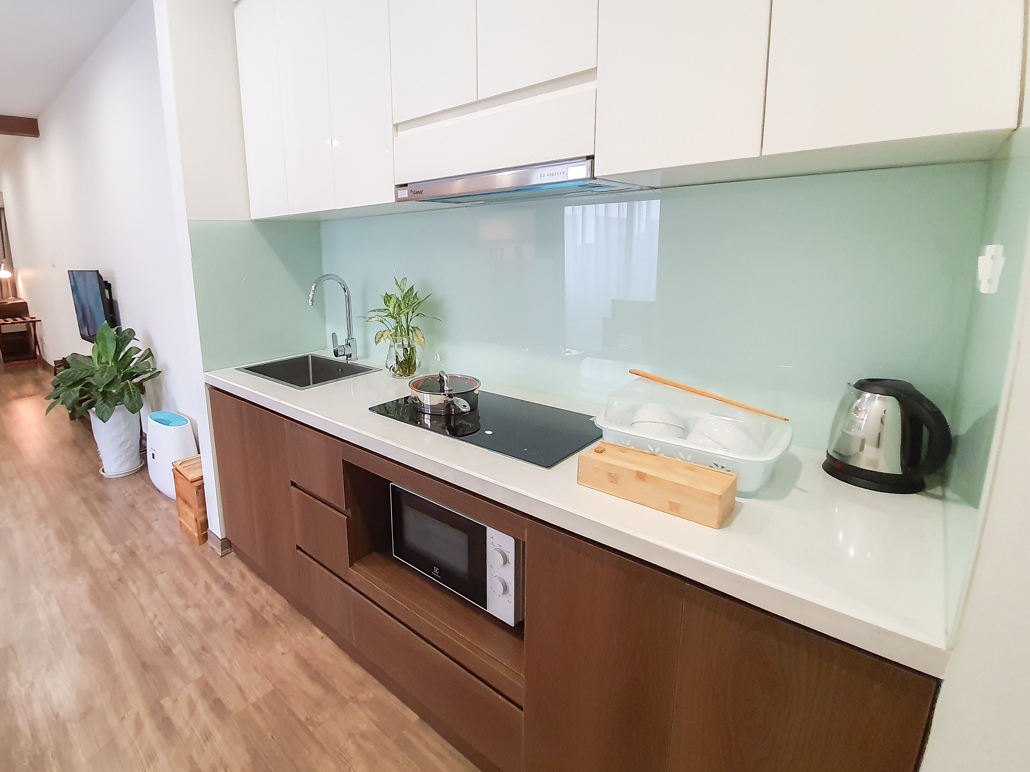 A modern kitchen with a sink, stove, and microwave. There is a plant and a kettle on the counter.