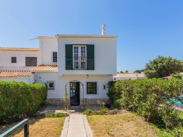 Un bâtiment blanc à deux étages, doté de volets verts, de fondations en pierre et d’un toit recouvert de tuiles.