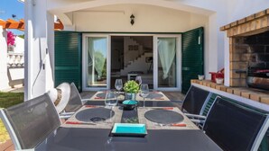 En udendørs terrasse med et spisebord, grill og en overdækket indgang til en bygning.