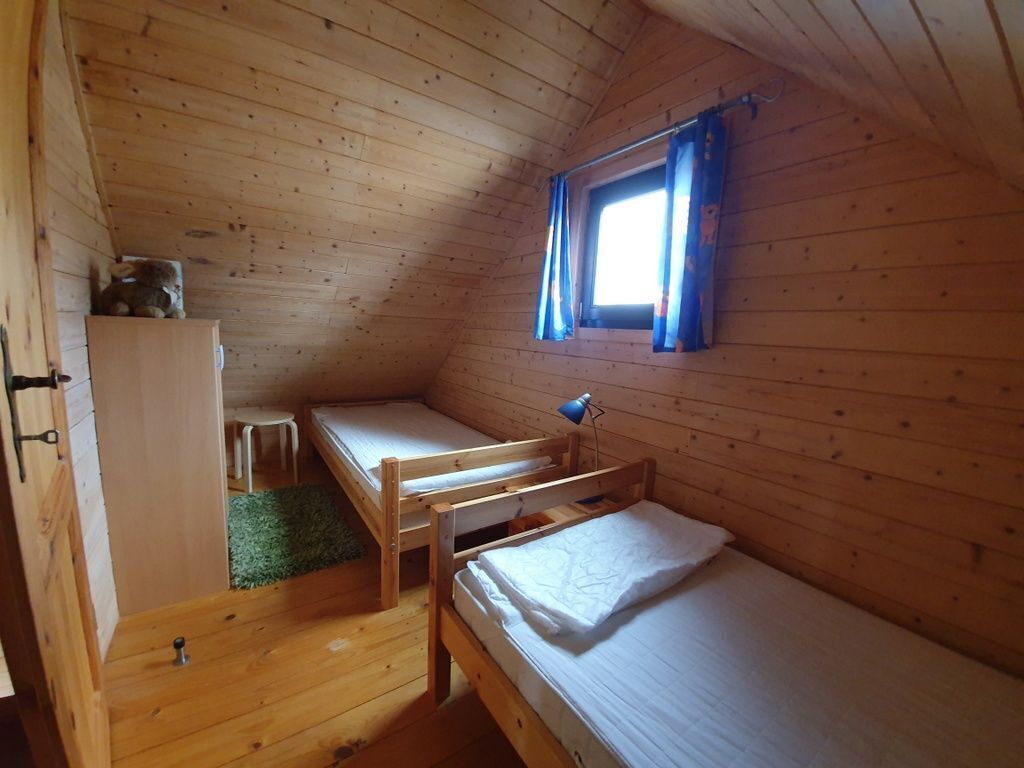 A small, wooden cabin room with bunk beds, a desk, and a window with curtains.
