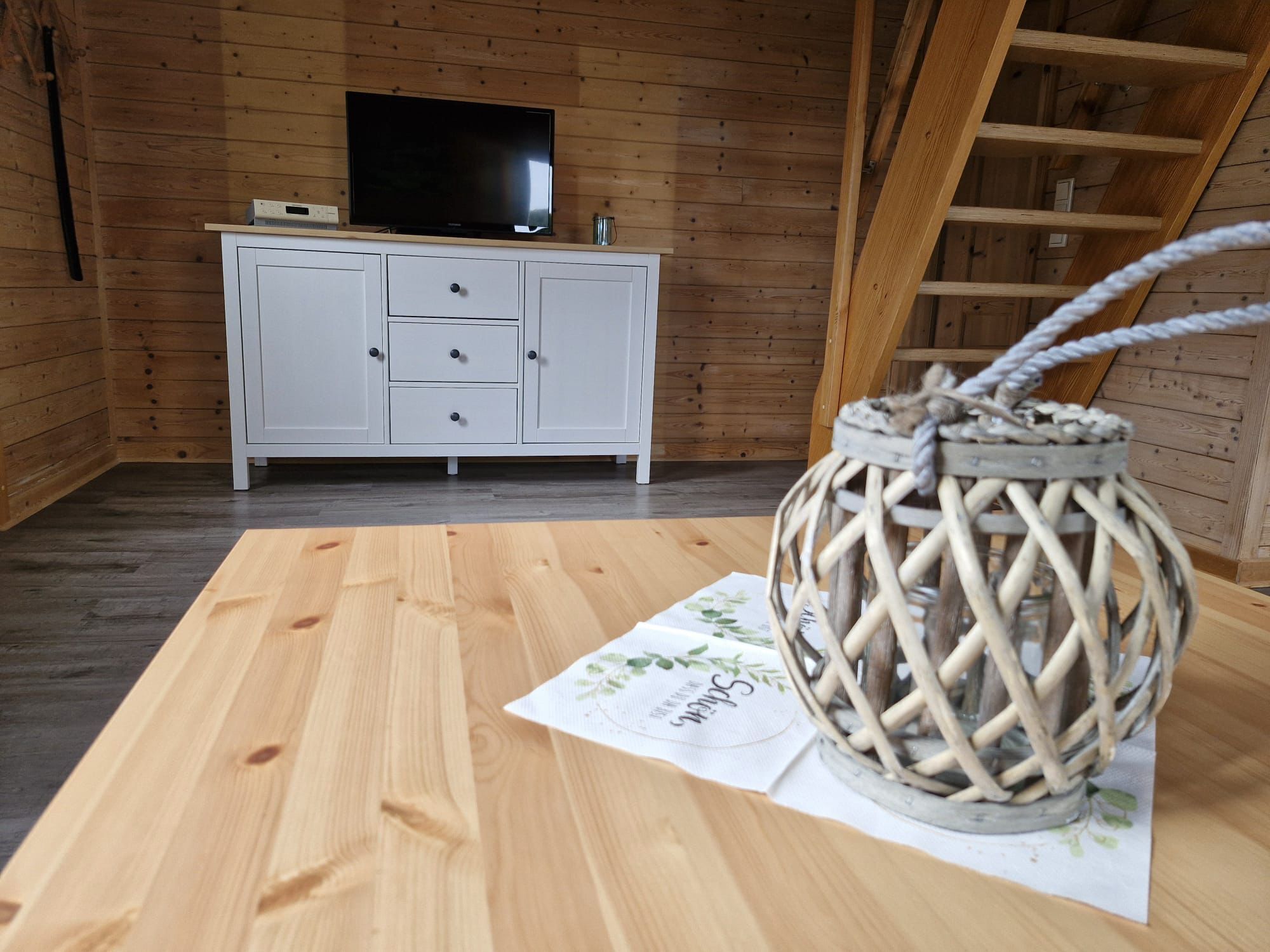 A wooden room with a white cabinet, a flat-screen TV, and a woven basket on a table.