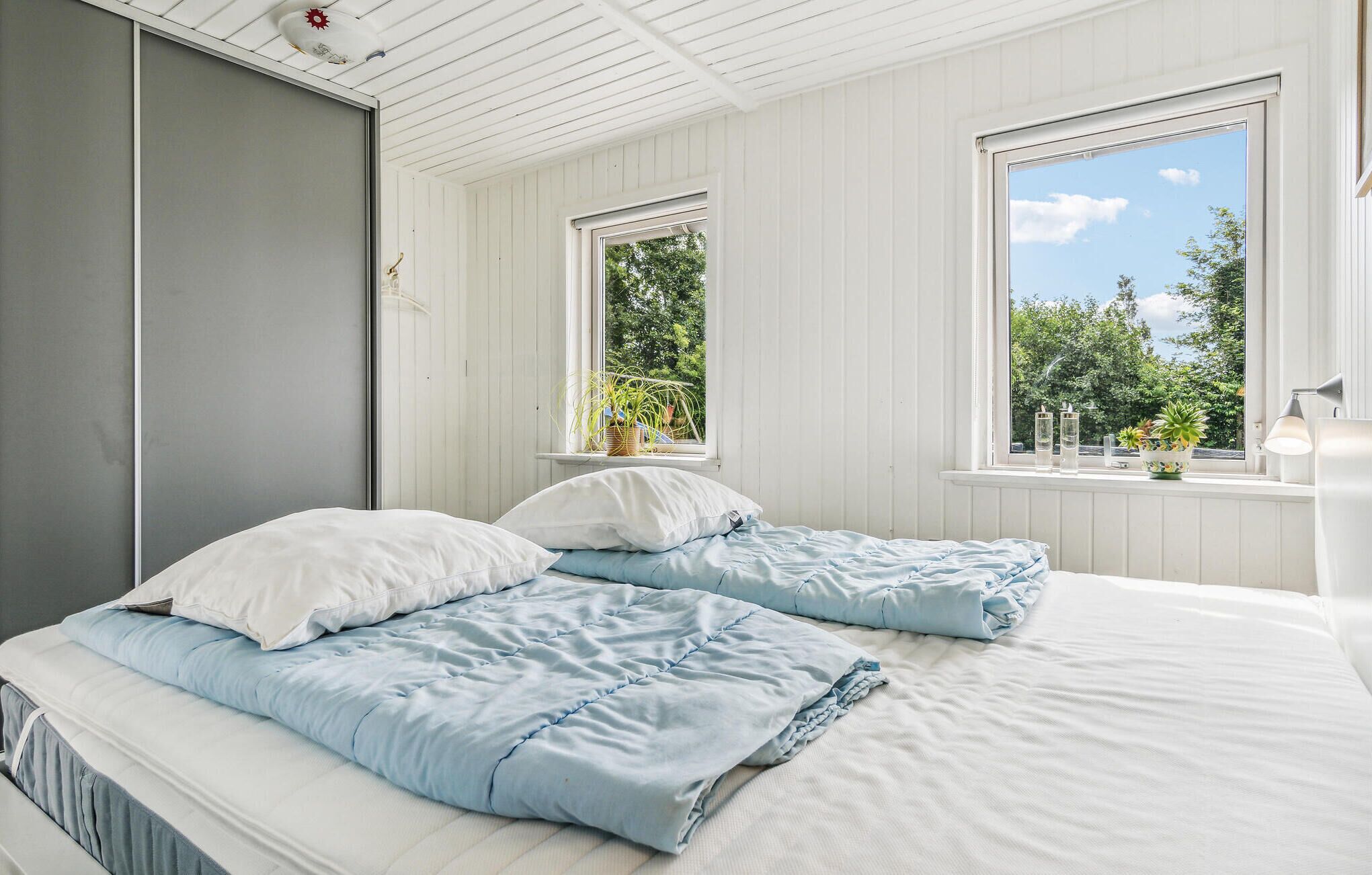 A bedroom with two beds, white walls, and large windows.