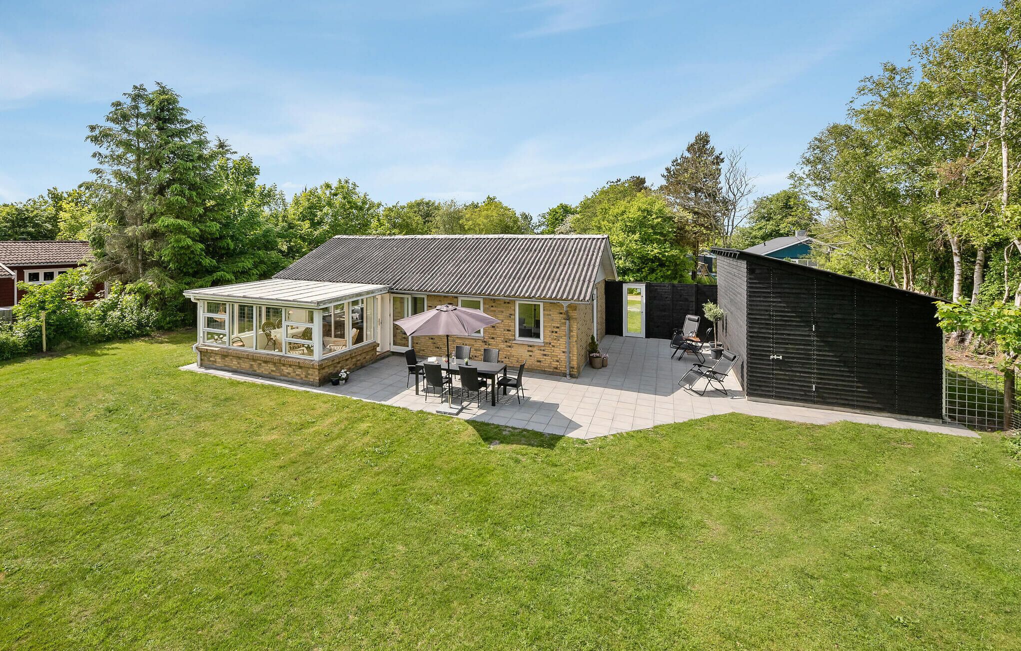 A house with a glass conservatory, a patio with outdoor furniture, and a separate shed.