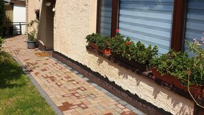 A building with a textured facade, a brick pathway, and flower boxes along the exterior wall.