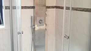 A modern bathroom with a glass-enclosed shower, a handheld showerhead, and a control panel.