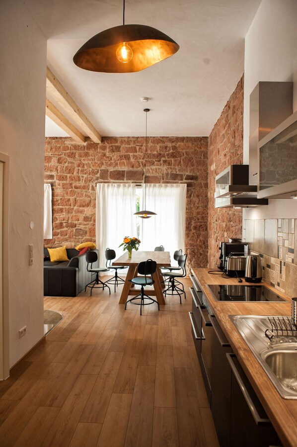 A modern kitchen with a brick wall, wooden flooring, and a dining area with a table and chairs.