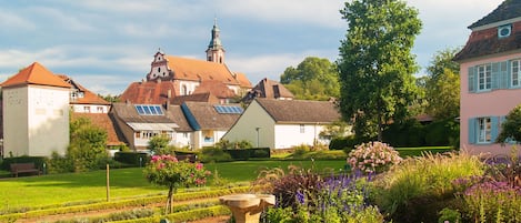A garden with a fountain, neatly trimmed hedges, and a building with a distinctive tower in the background.