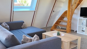 Un dormitorio estilo loft moderno con techo inclinado, una escalera de madera, un sofá, una mesa de centro y un televisor.