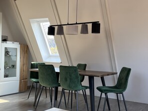 Uma sala de jantar com uma mesa e quatro cadeiras verdes, um armário de madeira e um claraboia.