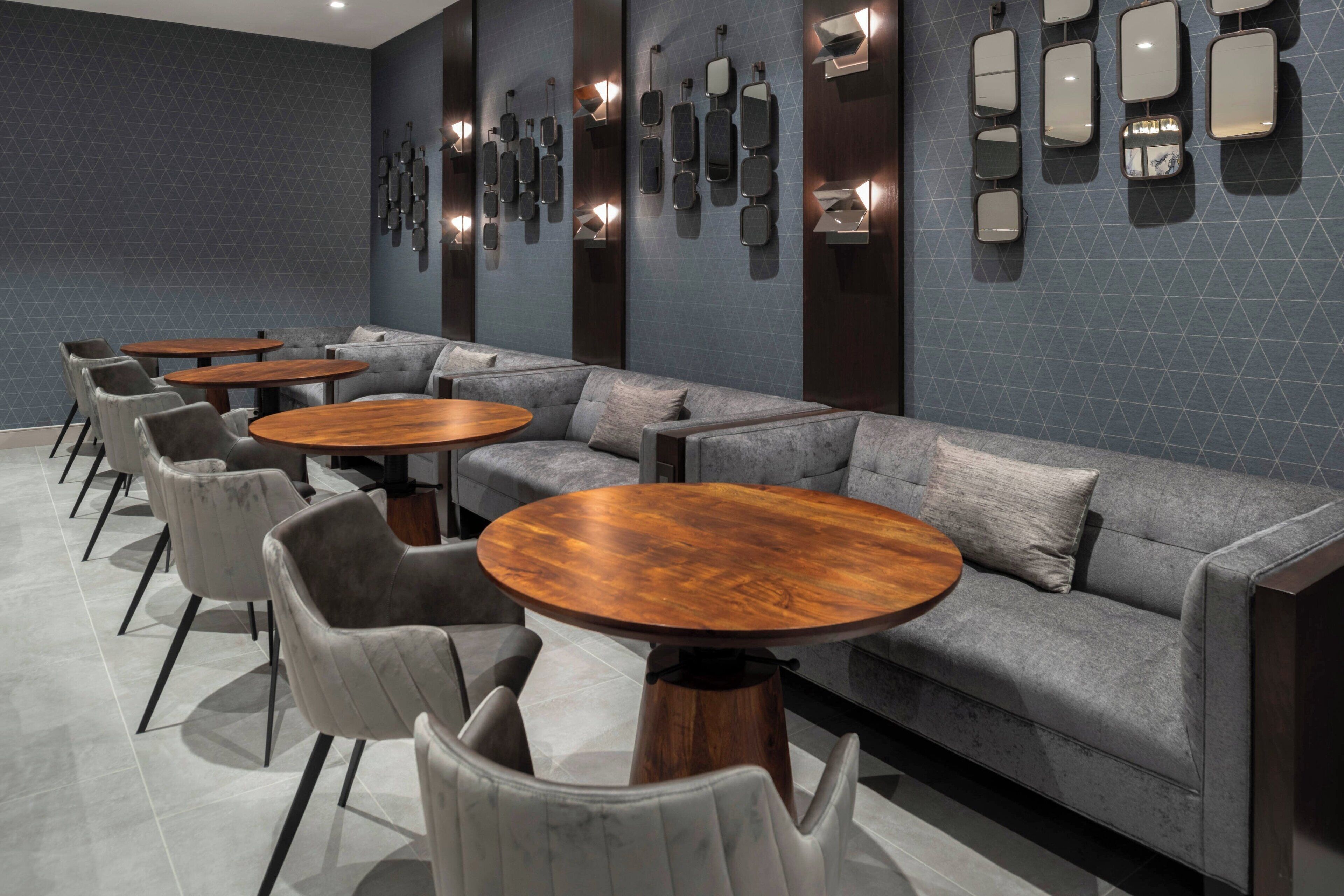 Ein stilvoller Lounge-Bereich mit grauen Sofas, runden Holztischen und grauen Sesseln.