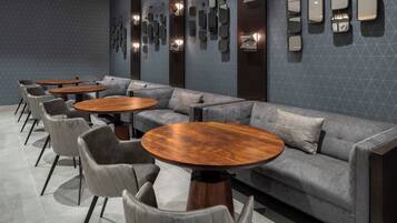 Ein stilvoller Lounge-Bereich mit grauen Sofas, runden Holztischen und grauen Sesseln.
