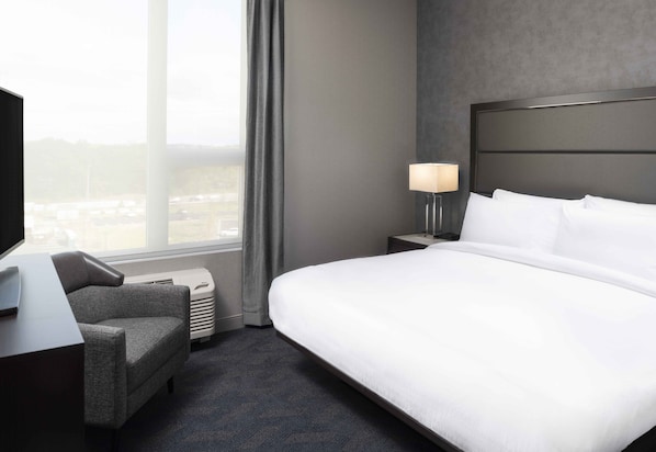 Une chambre d’hôtel avec un grand lit, un bureau avec une lampe, une chaise et une vue sur la ville par la fenêtre.
