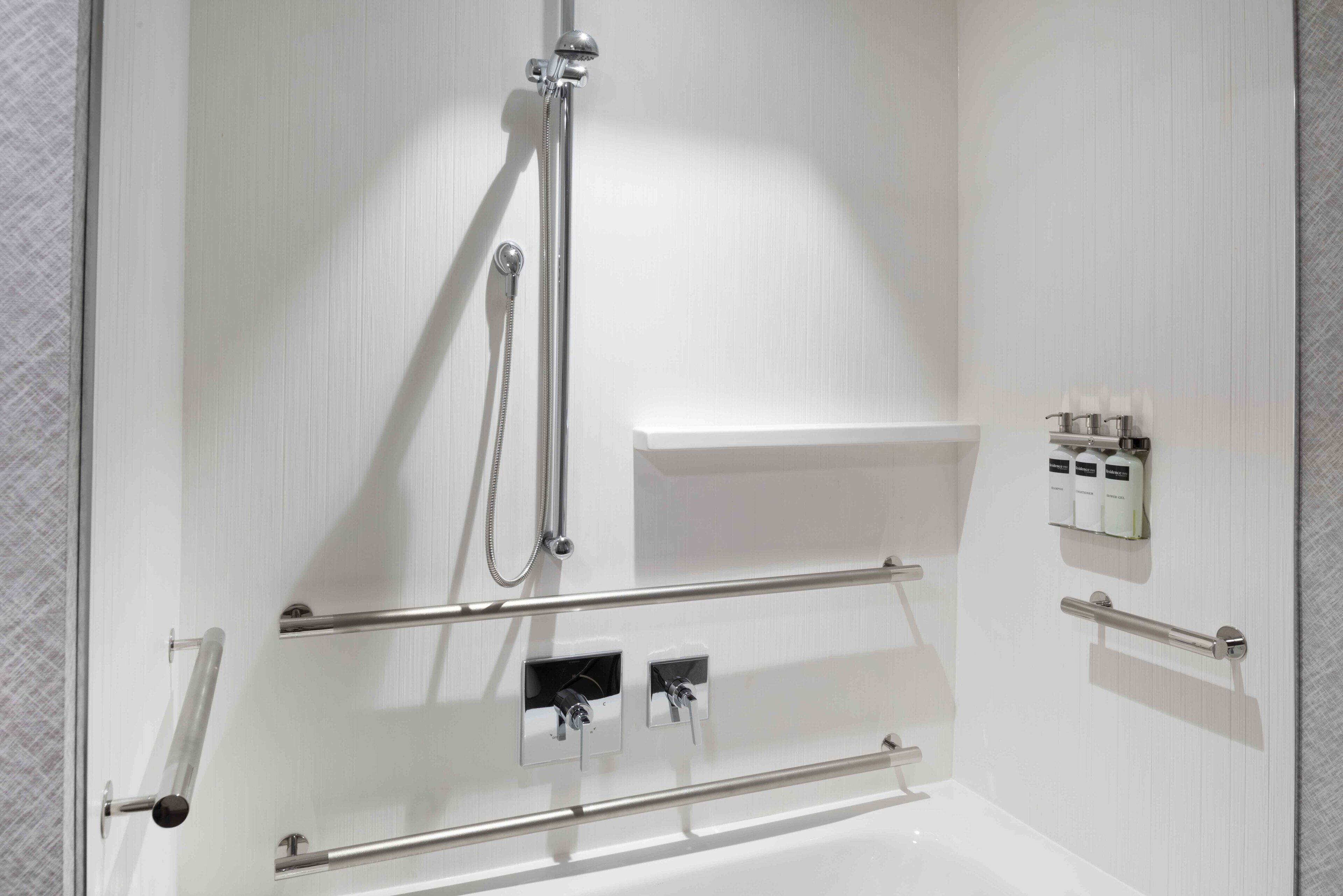 A modern bathroom with a white bathtub, a shower with a handheld showerhead, and a shelf with toiletries.