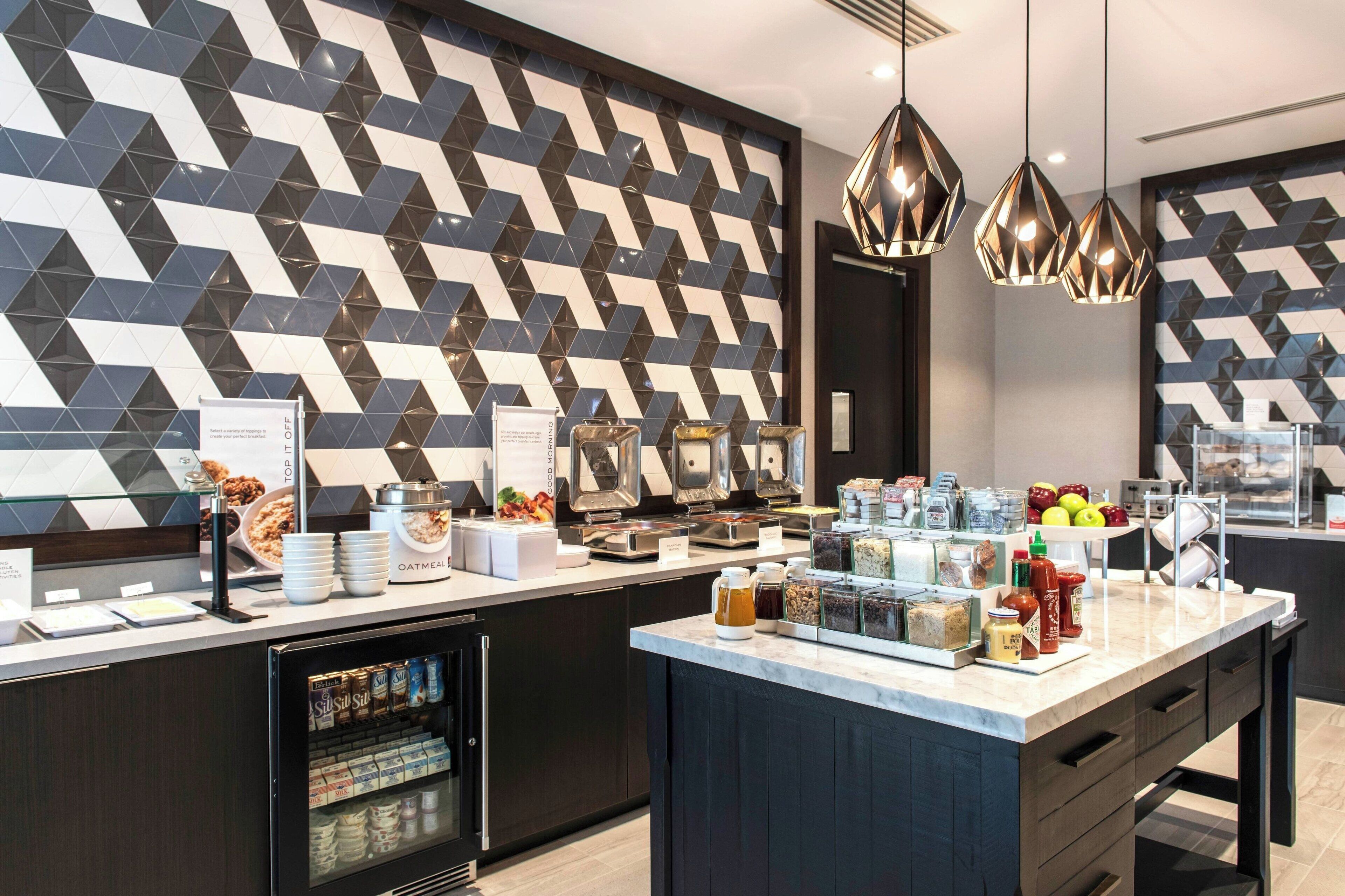 A modern breakfast bar with a geometric patterned wall, a variety of food items, and a coffee machine.