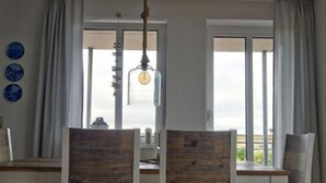 A dining area with wooden chairs and a table, large windows with curtains, and a hanging light fixture. - Wide view - ideally located family apartment with charm (Wangerooge)