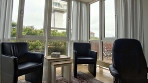 A room with large windows, two black chairs, a small table, and a view of buildings and greenery outside. - Wide view - ideally located family apartment with charm (Wangerooge)